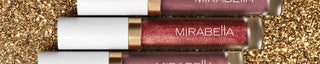 A banner image of Mirabella's lip glosses showcasing a sparkly shade with gold collar on a glitter background.